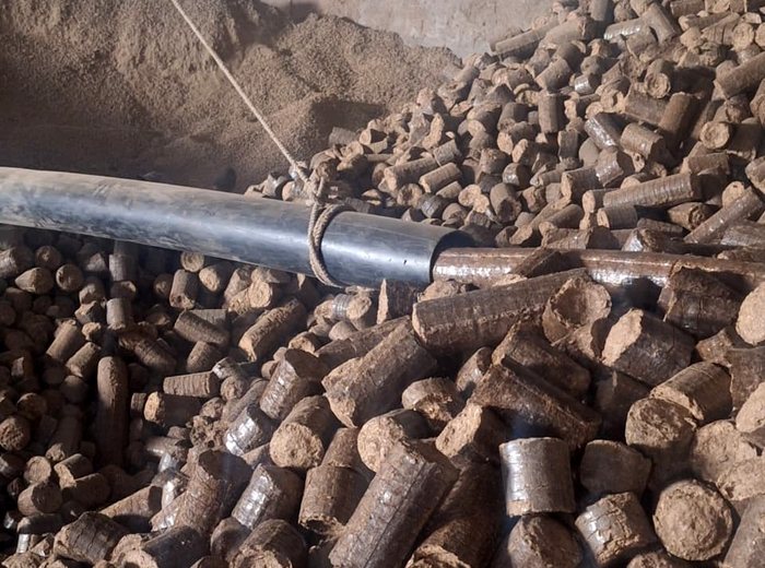 Freshly pressed biomass briquettes discharged beside the ground feedstock